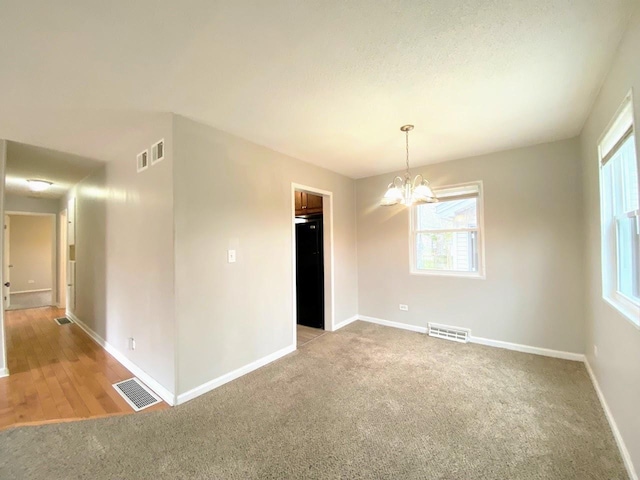 unfurnished room featuring light carpet, visible vents, an inviting chandelier, and a wealth of natural light