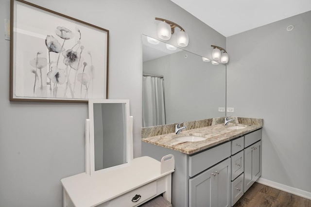 bathroom with a sink, baseboards, double vanity, and wood finished floors