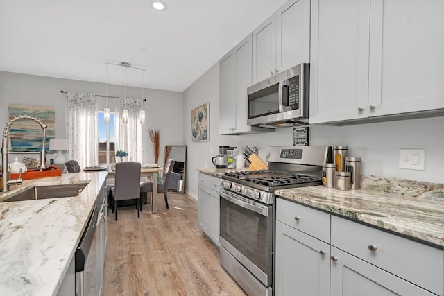 kitchen featuring light stone countertops, light wood-type flooring, a chandelier, appliances with stainless steel finishes, and a sink