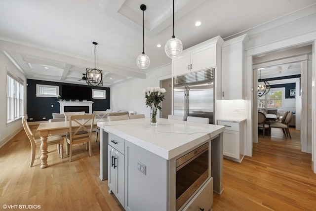 kitchen with recessed lighting, coffered ceiling, an inviting chandelier, light wood-style floors, and built in appliances
