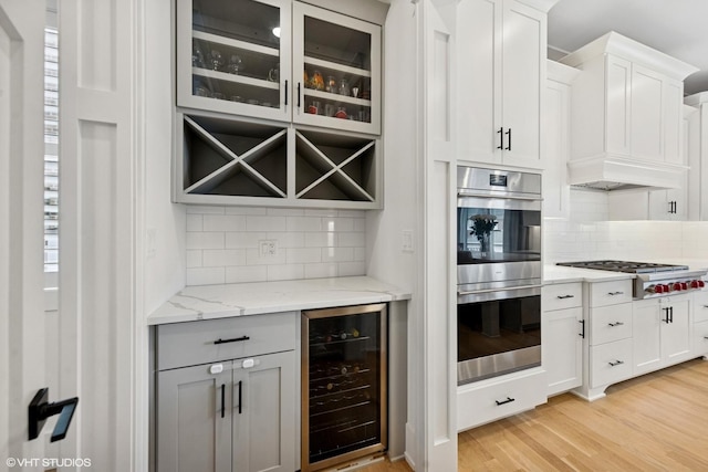 bar with backsplash, beverage cooler, appliances with stainless steel finishes, and light wood-style flooring