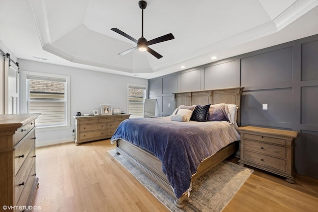 bedroom featuring a barn door, a decorative wall, a tray ceiling, and light wood-style floors