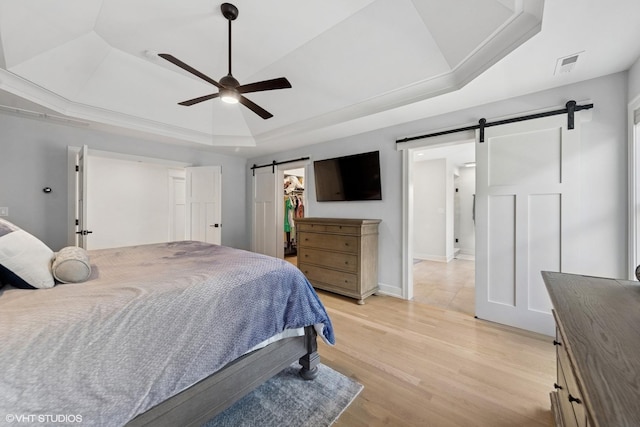 bedroom with a tray ceiling, a barn door, light wood-type flooring, visible vents, and a spacious closet