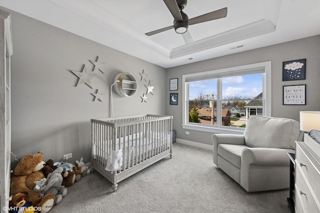 carpeted bedroom featuring a tray ceiling, visible vents, baseboards, a ceiling fan, and a nursery area