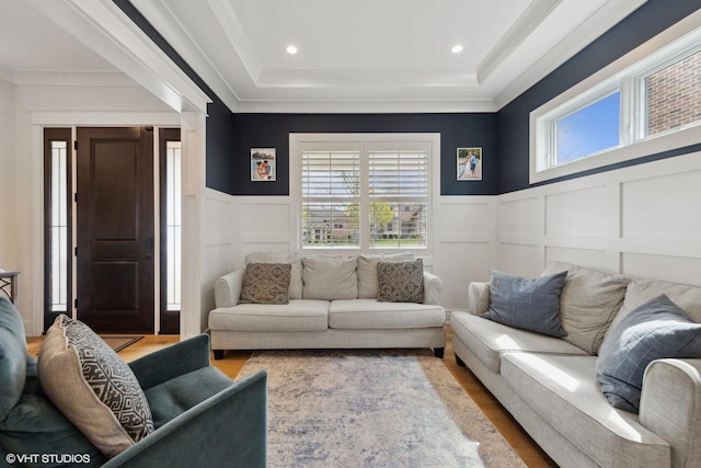 living area featuring a wainscoted wall, a raised ceiling, wood finished floors, a decorative wall, and ornamental molding