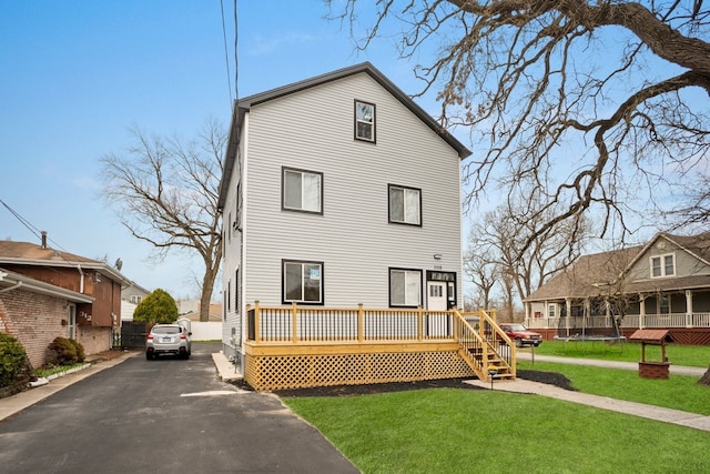 rear view of property featuring a yard, fence, a trampoline, and a deck