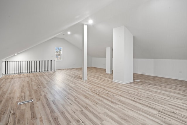 additional living space with light wood-style floors, visible vents, baseboards, and lofted ceiling
