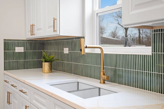 interior details with a sink, decorative backsplash, white cabinetry, and light stone counters