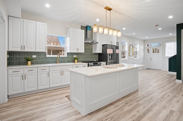 kitchen featuring wall chimney range hood, a center island, white cabinetry, appliances with stainless steel finishes, and a sink