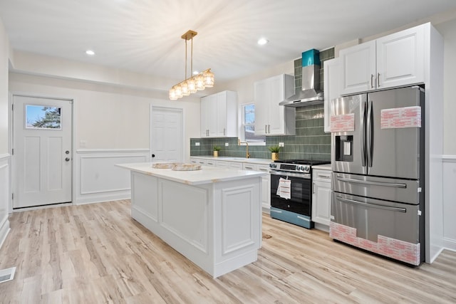 kitchen with white cabinets, wall chimney exhaust hood, light countertops, appliances with stainless steel finishes, and light wood finished floors