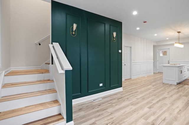 staircase with visible vents, a decorative wall, recessed lighting, wainscoting, and wood finished floors