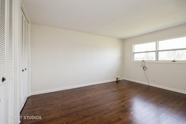 unfurnished bedroom featuring baseboards, two closets, and dark wood finished floors