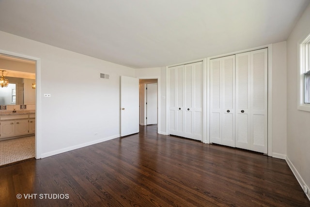 unfurnished bedroom with a notable chandelier, baseboards, visible vents, multiple closets, and dark wood finished floors