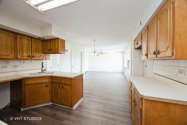 kitchen with a sink, dark wood-style flooring, a chandelier, brown cabinets, and decorative backsplash