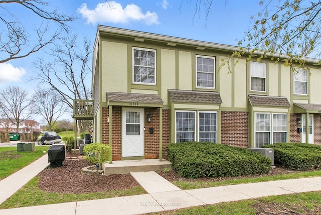 townhome / multi-family property featuring a shingled roof, brick siding, cooling unit, and stucco siding
