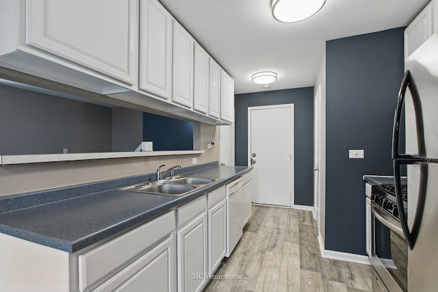 kitchen featuring dark countertops, a sink, stainless steel gas range, white cabinetry, and freestanding refrigerator
