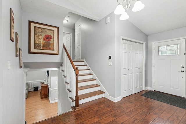 foyer with lofted ceiling, dark wood-style floors, stairs, a chandelier, and baseboards