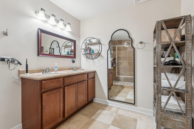 full bath featuring tiled shower, double vanity, and baseboards
