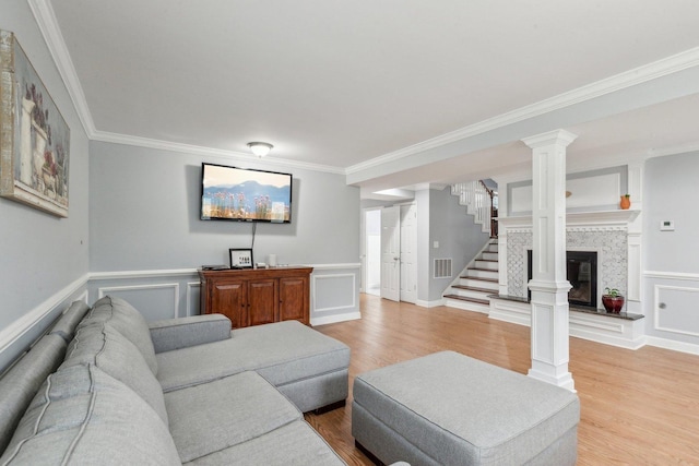 living room with crown molding, light wood-style flooring, stairs, wainscoting, and ornate columns