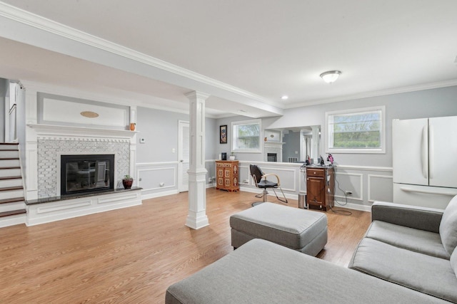 living room with a fireplace, ornamental molding, a decorative wall, ornate columns, and light wood-style floors