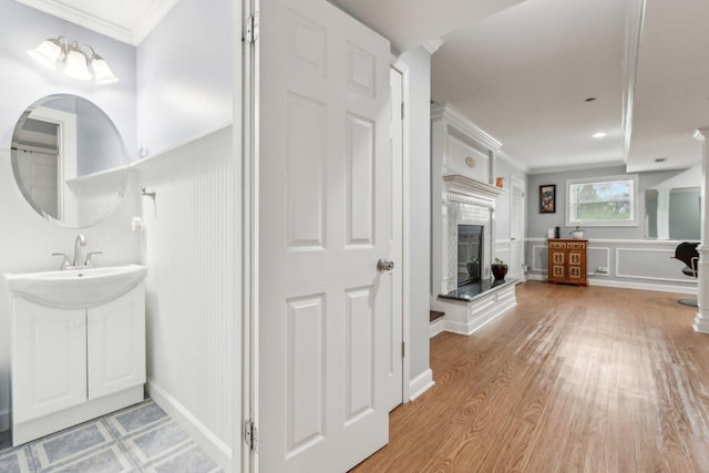 bathroom featuring a glass covered fireplace, crown molding, a decorative wall, wood finished floors, and vanity
