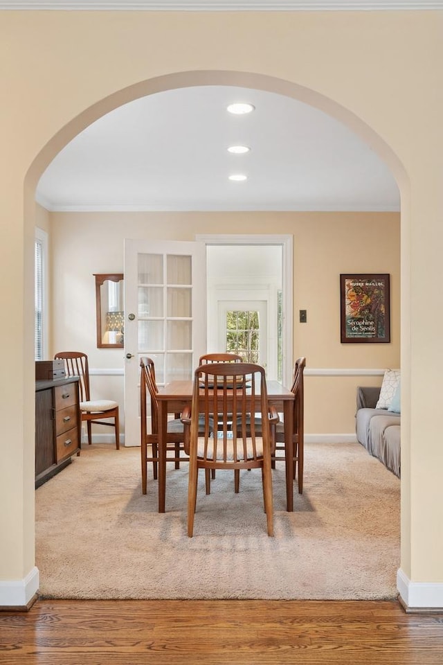 carpeted dining room with baseboards, arched walkways, wood finished floors, and ornamental molding