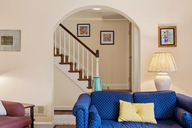 living room featuring visible vents, wood finished floors, baseboards, stairway, and arched walkways