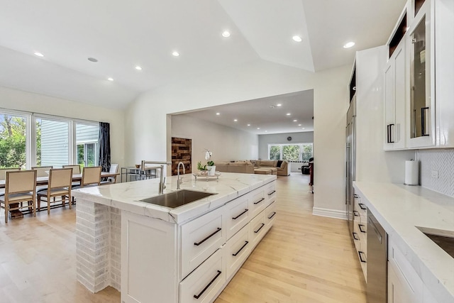 kitchen featuring light wood-style floors, a sink, glass insert cabinets, and vaulted ceiling