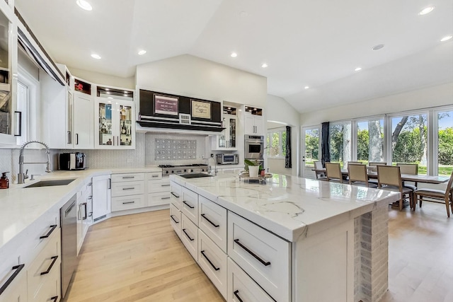 kitchen with a sink, light wood-style floors, decorative backsplash, light stone counters, and lofted ceiling