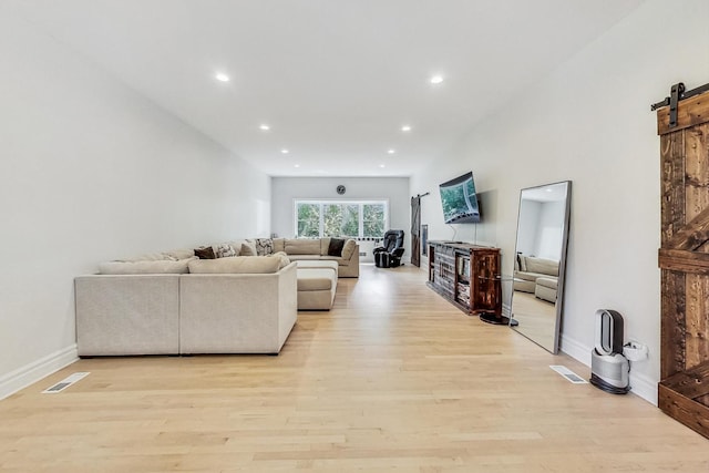 living room with light wood-type flooring, recessed lighting, visible vents, and a barn door