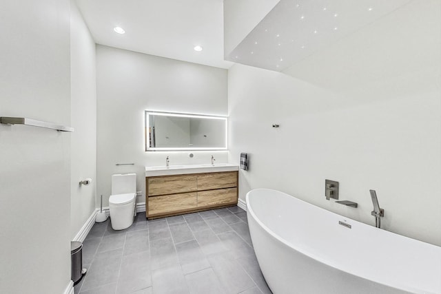 full bath featuring baseboards, a freestanding bath, toilet, double vanity, and tile patterned floors