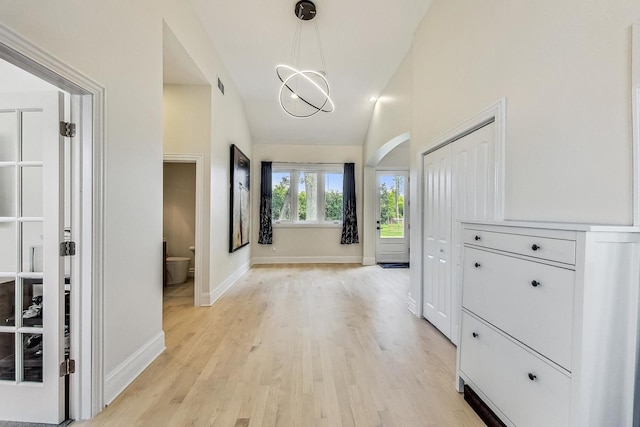 corridor featuring baseboards, vaulted ceiling, light wood-style floors, visible vents, and arched walkways