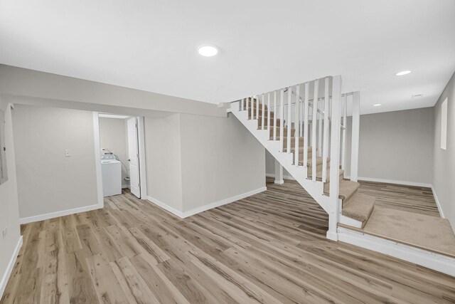 unfurnished living room featuring washer / clothes dryer, baseboards, light wood finished floors, and stairs