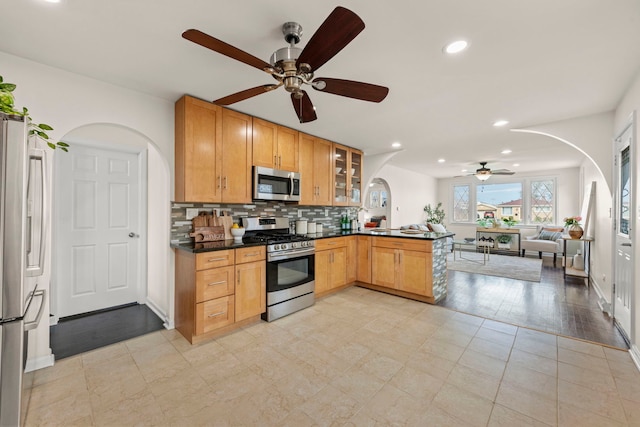 kitchen featuring arched walkways, appliances with stainless steel finishes, dark countertops, and ceiling fan