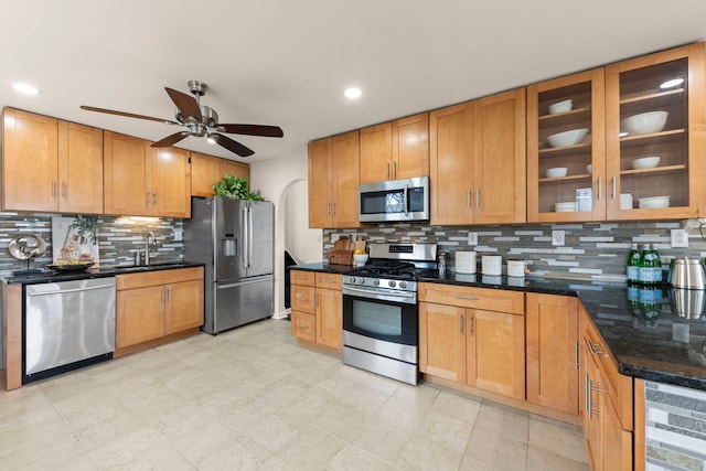 kitchen with appliances with stainless steel finishes, a sink, arched walkways, a ceiling fan, and decorative backsplash