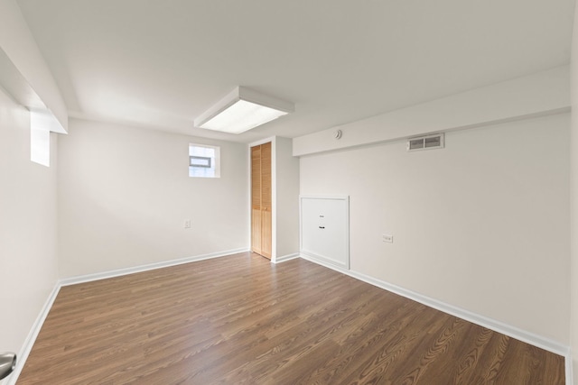 basement with baseboards, visible vents, and dark wood-style floors