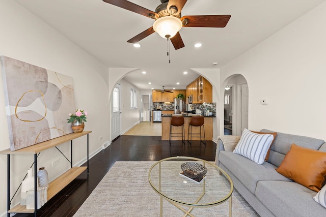 living room with wood finished floors, baseboards, ceiling fan, recessed lighting, and arched walkways