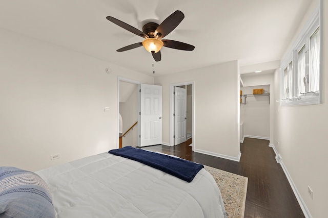 bedroom featuring ceiling fan, a walk in closet, baseboards, and wood finished floors
