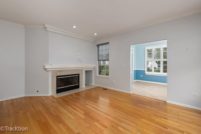 unfurnished living room with a tiled fireplace, ornamental molding, baseboards, and light wood finished floors