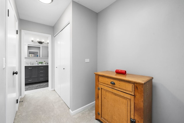 corridor with baseboards, light carpet, and a sink