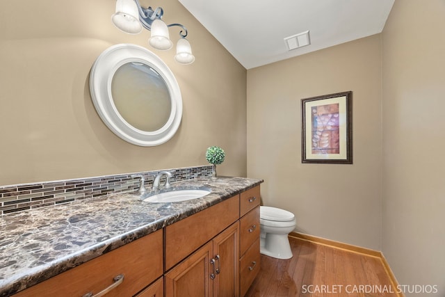 bathroom featuring vanity, toilet, baseboards, wood finished floors, and visible vents