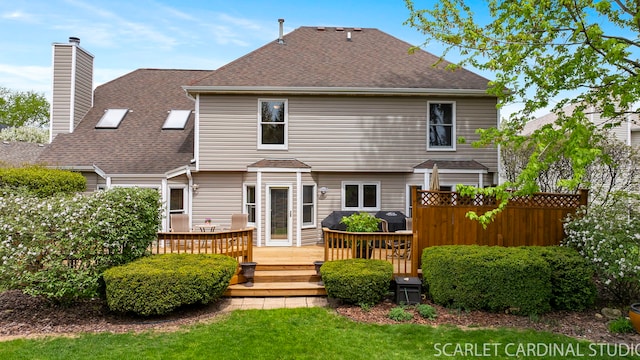 back of property with a shingled roof, a chimney, and a deck