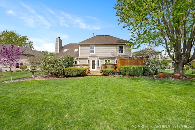 rear view of house featuring a chimney, a deck, fence, a yard, and a shingled roof