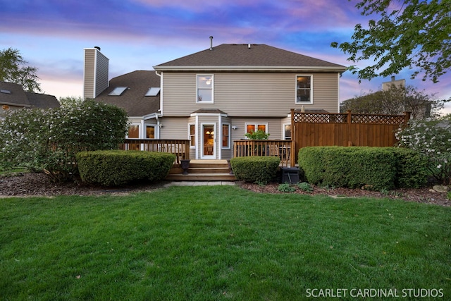 back of property featuring a shingled roof, a yard, a chimney, and a deck