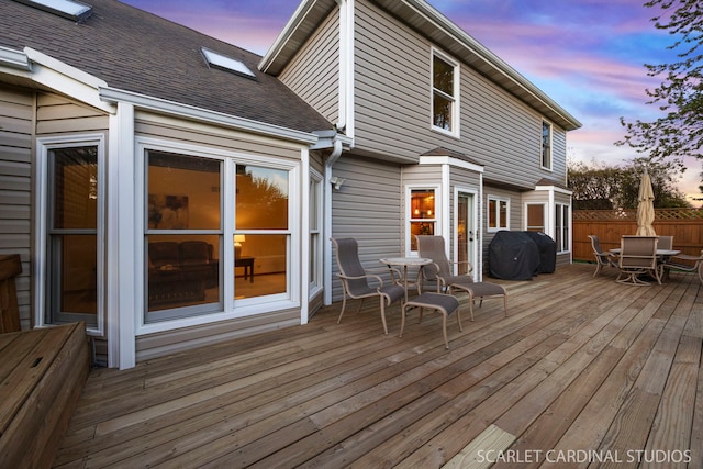 deck at dusk featuring area for grilling, fence, and outdoor dining space