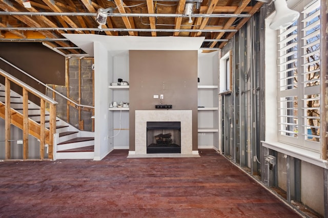 unfurnished living room featuring a tile fireplace, stairs, and wood finished floors