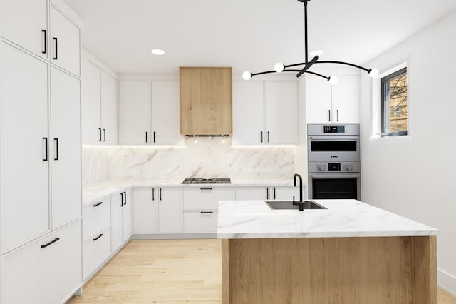 kitchen featuring a sink, stainless steel appliances, backsplash, light wood finished floors, and light stone countertops