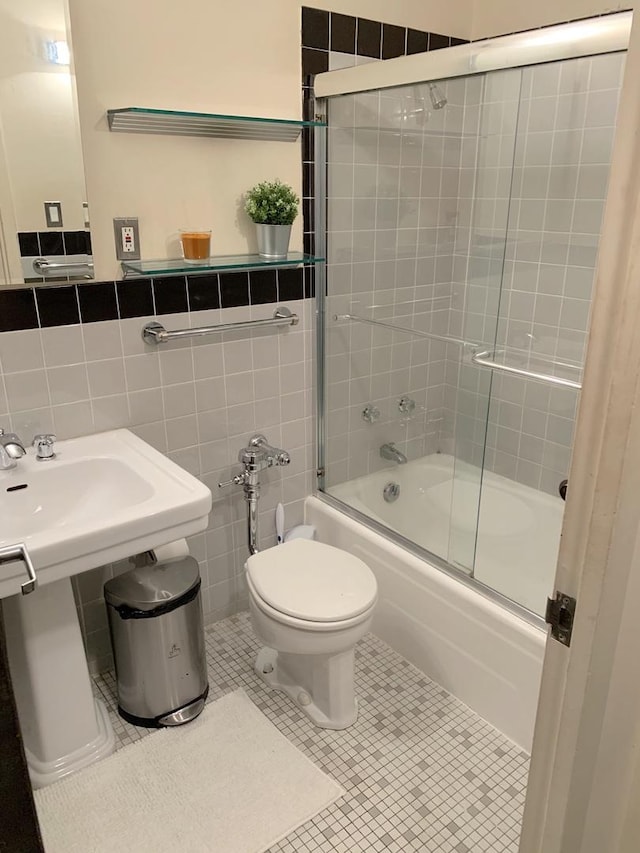 bathroom with bath / shower combo with glass door, a wainscoted wall, tile walls, and toilet