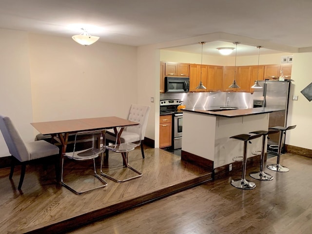 kitchen with dark wood-style flooring, baseboards, dark countertops, a breakfast bar area, and appliances with stainless steel finishes