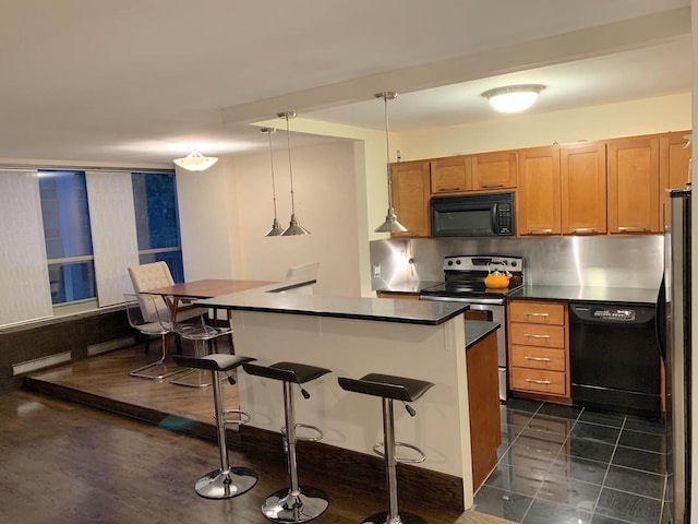 kitchen featuring dark countertops, brown cabinetry, black appliances, and a kitchen breakfast bar